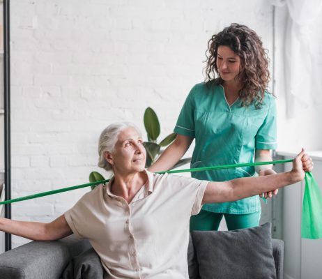 senior-woman-with-stretch-band-being-assist-by-female-physiotherapist
